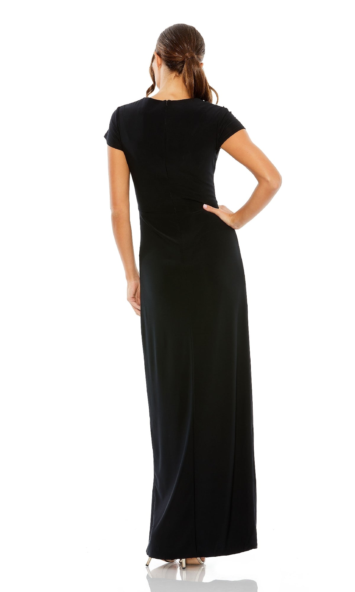 A woman, facing away from the camera, wears the Mac Duggal 11670 short sleeve black formal dress and beige heels against a white background.